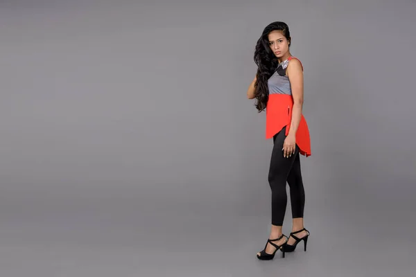 stock image Studio shot of a young, beautiful Indian female model in casual wear wearing red and grey designer top and blue jeans against grey background. Female model. Fashion Portrait.