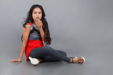 Gri arka planda kırmızı ve gri renkli ve mavi kot pantolon giyen, gündelik giyimli genç ve güzel bir Hintli kadın modelin stüdyo fotoğrafı. Kadın manken. Moda Portresi.