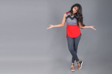 Gri arka planda kırmızı ve gri renkli ve mavi kot pantolon giyen, gündelik giyimli genç ve güzel bir Hintli kadın modelin stüdyo fotoğrafı. Kadın manken. Moda Portresi.