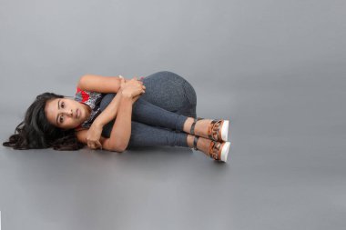 Gri arka planda kırmızı ve gri renkli ve mavi kot pantolon giyen, gündelik giyimli genç ve güzel bir Hintli kadın modelin stüdyo fotoğrafı. Kadın manken. Moda Portresi.