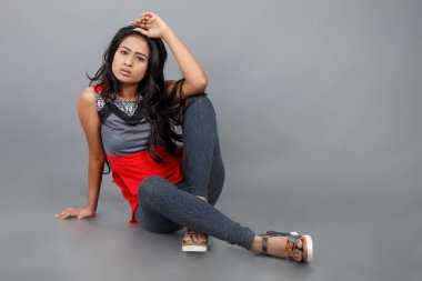 Gri arka planda kırmızı ve gri renkli ve mavi kot pantolon giyen, gündelik giyimli genç ve güzel bir Hintli kadın modelin stüdyo fotoğrafı. Kadın manken. Moda Portresi.