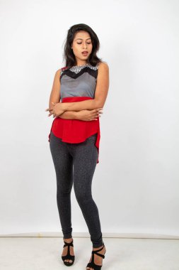 Genç, güzel bir Hintli kadın modelin gündelik kıyafetleriyle stüdyo fotoğrafı. Kırmızı ve gri tasarımcı bluzu ve beyaz arka planda siyah kot pantolon giyiyor. Kadın manken. Moda Portresi.