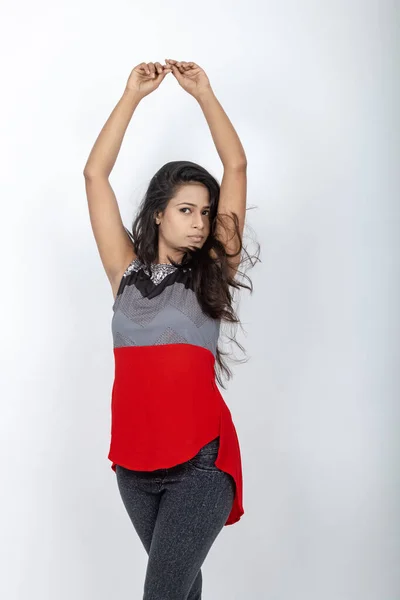 Studio shot of a young, beautiful Indian female model in casual wear wearing red and grey designer top and black jeans against white background. Female model. Fashion Portrait.
