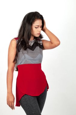 Genç, güzel bir Hintli kadın modelin gündelik kıyafetleriyle stüdyo fotoğrafı. Kırmızı ve gri tasarımcı bluzu ve beyaz arka planda siyah kot pantolon giyiyor. Kadın manken. Moda Portresi.