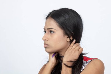 Genç bir Hintli kadın model, günlük kıyafetleriyle saçını tarıyor. Kırmızı ve gri tasarımcı bluzu ve beyaz arka planda siyah kot pantolon giyiyor. Reklam çekimi.