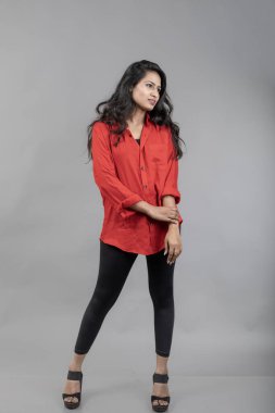 Gri arka plan karşısında gündelik giyimli Hintli genç bayan model - stok fotoğrafı. Kırmızı gömlek ve siyah kot giyen uzun siyah saçlı bir manken..