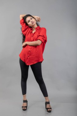 Gri arka plan karşısında gündelik giyimli Hintli genç bayan model - stok fotoğrafı. Kırmızı gömlek ve siyah kot giyen uzun siyah saçlı bir manken..