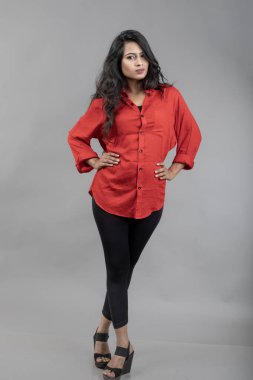 Gri arka plan karşısında gündelik giyimli Hintli genç bayan model - stok fotoğrafı. Kırmızı gömlek ve siyah kot giyen uzun siyah saçlı bir manken..