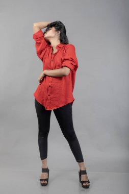 Gri arka plan karşısında gündelik giyimli Hintli genç bayan model - stok fotoğrafı. Kırmızı gömlek ve siyah kot giyen uzun siyah saçlı bir manken..