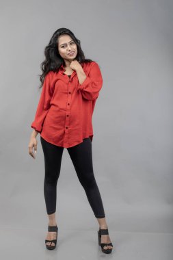 Gri arka plan karşısında gündelik giyimli Hintli genç bayan model - stok fotoğrafı. Kırmızı gömlek ve siyah kot giyen uzun siyah saçlı bir manken..