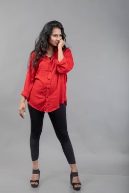 Gri arka plan karşısında gündelik giyimli Hintli genç bayan model - stok fotoğrafı. Kırmızı gömlek ve siyah kot giyen uzun siyah saçlı bir manken..