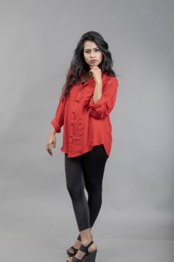 Gri arka plan karşısında gündelik giyimli Hintli genç bayan model - stok fotoğrafı. Kırmızı gömlek ve siyah kot giyen uzun siyah saçlı bir manken..