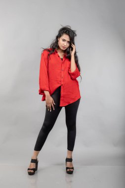 Gri arka plan karşısında gündelik giyimli Hintli genç bayan model - stok fotoğrafı. Kırmızı gömlek ve siyah kot giyen uzun siyah saçlı bir manken..