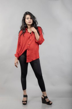 Gri arka plan karşısında gündelik giyimli Hintli genç bayan model - stok fotoğrafı. Kırmızı gömlek ve siyah kot giyen uzun siyah saçlı bir manken..