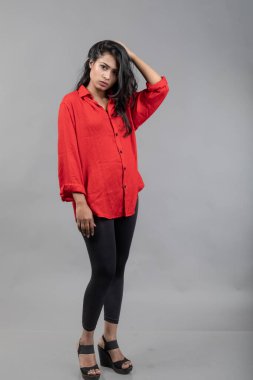 Gri arka plan karşısında gündelik giyimli Hintli genç bayan model - stok fotoğrafı. Kırmızı gömlek ve siyah kot giyen uzun siyah saçlı bir manken..