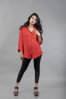 Gri arka plan karşısında gündelik giyimli Hintli genç bayan model - stok fotoğrafı. Kırmızı gömlek ve siyah kot giyen uzun siyah saçlı bir manken..