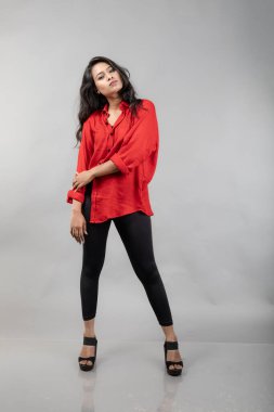 Gri arka plan karşısında gündelik giyimli Hintli genç bayan model - stok fotoğrafı. Kırmızı gömlek ve siyah kot giyen uzun siyah saçlı bir manken..