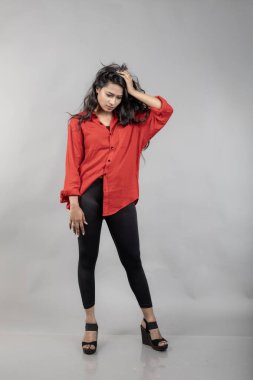 Gri arka plan karşısında gündelik giyimli Hintli genç bayan model - stok fotoğrafı. Kırmızı gömlek ve siyah kot giyen uzun siyah saçlı bir manken..