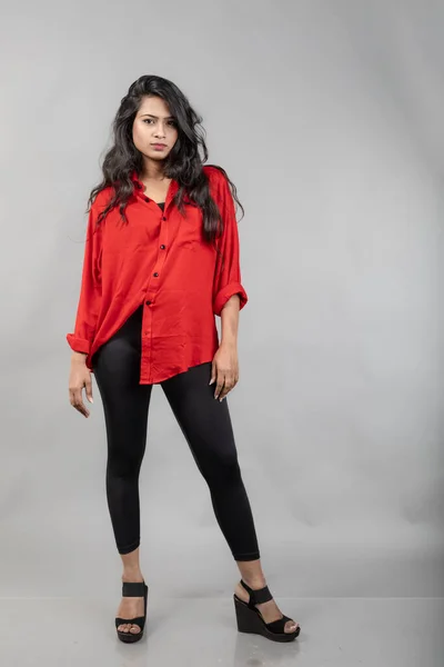 Indian young female model in casual wear against grey background - stock photo. Long black haired model wearing red shirt and black jeans.