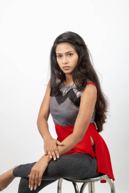Genç, güzel bir Hintli kadın modelin gündelik kıyafetleriyle stüdyo fotoğrafı. Kırmızı ve gri tasarımcı bluzu ve beyaz arka planda siyah kot pantolon giyiyor. Kadın manken. Moda Portresi.