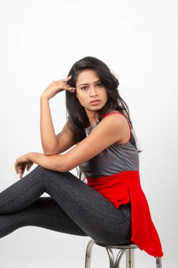 Genç, güzel bir Hintli kadın modelin gündelik kıyafetleriyle stüdyo fotoğrafı. Kırmızı ve gri tasarımcı bluzu ve beyaz arka planda siyah kot pantolon giyiyor. Kadın manken. Moda Portresi.