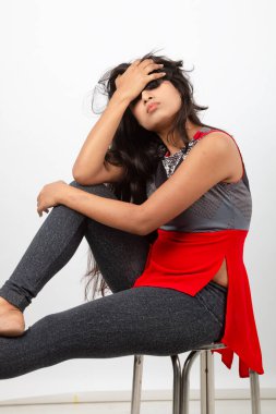 Genç, güzel bir Hintli kadın modelin gündelik kıyafetleriyle stüdyo fotoğrafı. Kırmızı ve gri tasarımcı bluzu ve beyaz arka planda siyah kot pantolon giyiyor. Kadın manken. Moda Portresi.