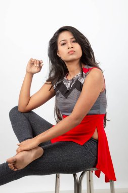 Genç, güzel bir Hintli kadın modelin gündelik kıyafetleriyle stüdyo fotoğrafı. Kırmızı ve gri tasarımcı bluzu ve beyaz arka planda siyah kot pantolon giyiyor. Kadın manken. Moda Portresi.