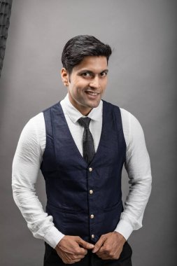 Gri arka planda resmi giyinmiş neşeli, genç ve yakışıklı Hintli iş adamının stüdyo çekimi. Şirket erkek modeli. Moda Portresi.