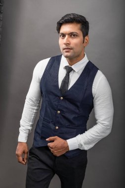 Gri arka planda resmi giyinmiş neşeli, genç ve yakışıklı Hintli iş adamının stüdyo çekimi. Şirket erkek modeli. Moda Portresi.