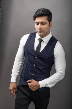 Gri arka planda resmi giyinmiş neşeli, genç ve yakışıklı Hintli iş adamının stüdyo çekimi. Şirket erkek modeli. Moda Portresi.