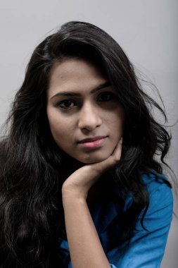 Gri arkaplanlı, mavi gömlekli Hintli genç manken. Stok fotoğrafı. Uzun siyah saç modeli mavi gömlek giyiyor..