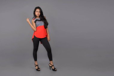 Genç, güzel bir Hintli kadın modelin gündelik kıyafetleriyle stüdyo fotoğrafı. Kırmızı ve gri tasarımcı bluzu ve beyaz arka planda siyah kot pantolon giyiyor. Kadın manken. Moda Portresi.