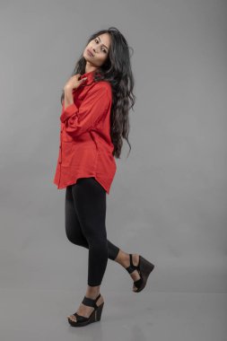 Gri arka plan karşısında gündelik giyimli Hintli genç bayan model - stok fotoğrafı. Kırmızı gömlek ve siyah kot giyen uzun siyah saçlı bir manken..