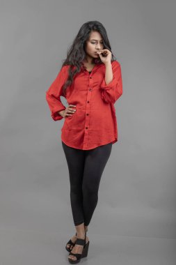 Gri arka plan karşısında gündelik giyimli Hintli genç bayan model - stok fotoğrafı. Kırmızı gömlek ve siyah kot giyen uzun siyah saçlı bir manken..