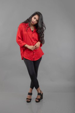 Gri arka plan karşısında gündelik giyimli Hintli genç bayan model - stok fotoğrafı. Kırmızı gömlek ve siyah kot giyen uzun siyah saçlı bir manken..