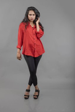 Gri arka plan karşısında gündelik giyimli Hintli genç bayan model - stok fotoğrafı. Kırmızı gömlek ve siyah kot giyen uzun siyah saçlı bir manken..