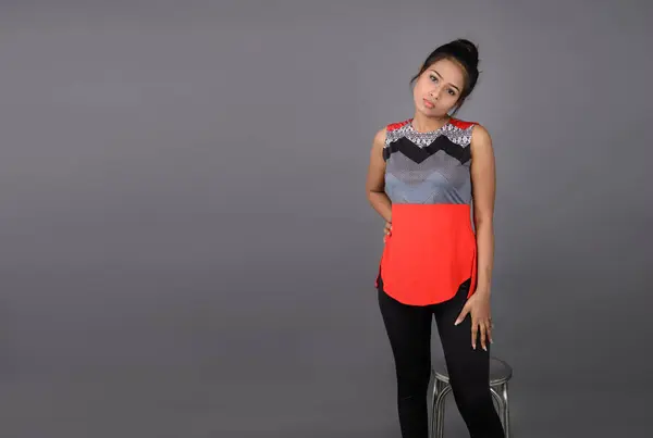 Studio shot of a young, beautiful Indian female model in casual wear wearing red and grey designer top and black jeans against white background. Female model. Fashion Portrait.