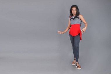 Genç, güzel bir Hintli kadın modelin gündelik kıyafetleriyle stüdyo fotoğrafı. Kırmızı ve gri tasarımcı bluzu ve beyaz arka planda siyah kot pantolon giyiyor. Kadın manken. Moda Portresi.