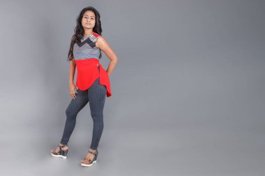 Genç, güzel bir Hintli kadın modelin gündelik kıyafetleriyle stüdyo fotoğrafı. Kırmızı ve gri tasarımcı bluzu ve beyaz arka planda siyah kot pantolon giyiyor. Kadın manken. Moda Portresi.