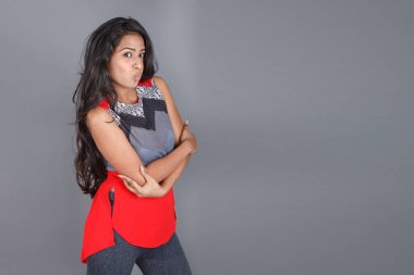 Genç, güzel bir Hintli kadın modelin gündelik kıyafetleriyle stüdyo fotoğrafı. Kırmızı ve gri tasarımcı bluzu ve beyaz arka planda siyah kot pantolon giyiyor. Kadın manken. Moda Portresi.