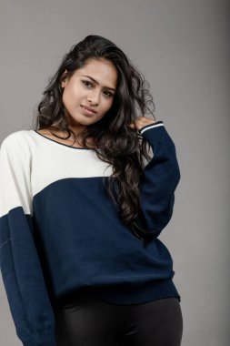 Gri arka planda günlük kışlık giysili Hintli genç bayan model. Siyah tayt giyen uzun siyah saçlı bir manken, mavi beyaz bir kazak..