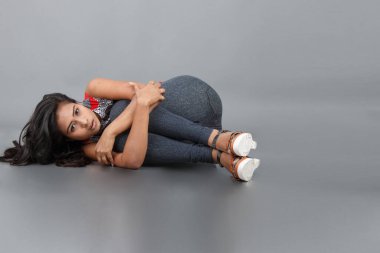 Gri arka planda kırmızı ve gri renkli ve mavi kot pantolon giyen, gündelik giyimli genç ve güzel bir Hintli kadın modelin stüdyo fotoğrafı. Kadın manken. Moda Portresi.