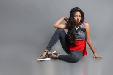 Genç, güzel bir Hintli kadın modelin gündelik kıyafetleriyle stüdyo fotoğrafı. Kırmızı ve gri tasarımcı bluzu ve beyaz arka planda siyah kot pantolon giyiyor. Kadın manken. Moda Portresi.