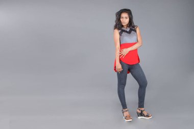 Genç, güzel bir Hintli kadın modelin gündelik kıyafetleriyle stüdyo fotoğrafı. Kırmızı ve gri tasarımcı bluzu ve beyaz arka planda siyah kot pantolon giyiyor. Kadın manken. Moda Portresi.