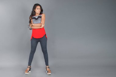 Genç, güzel bir Hintli kadın modelin gündelik kıyafetleriyle stüdyo fotoğrafı. Kırmızı ve gri tasarımcı bluzu ve beyaz arka planda siyah kot pantolon giyiyor. Kadın manken. Moda Portresi.