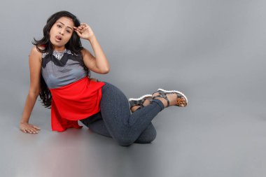 Gri arka planda kırmızı ve gri renkli ve mavi kot pantolon giyen, gündelik giyimli genç ve güzel bir Hintli kadın modelin stüdyo fotoğrafı. Kadın manken. Moda Portresi.