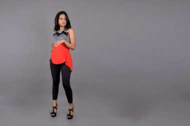 Genç, güzel bir Hintli kadın modelin gündelik kıyafetleriyle stüdyo fotoğrafı. Kırmızı ve gri tasarımcı bluzu ve beyaz arka planda siyah kot pantolon giyiyor. Kadın manken. Moda Portresi.