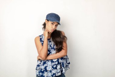 Genç ve güzel bir Hintli kadın modelin günlük spor kıyafetleri içinde beyaz arka planda mavi-beyaz bluz, mavi kot pantolon ve mavi başlık giyerken çekilmiş bir fotoğraf. Kadın manken. Moda Portresi.