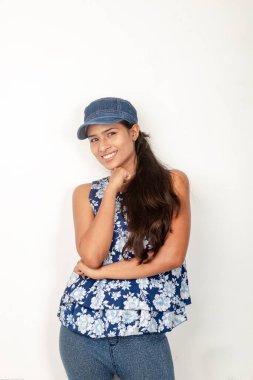 Genç ve güzel bir Hintli kadın modelin günlük spor kıyafetleri içinde beyaz arka planda mavi-beyaz bluz, mavi kot pantolon ve mavi başlık giyerken çekilmiş bir fotoğraf. Kadın manken. Moda Portresi.