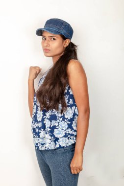 Genç ve güzel bir Hintli kadın modelin günlük spor kıyafetleri içinde beyaz arka planda mavi-beyaz bluz, mavi kot pantolon ve mavi başlık giyerken çekilmiş bir fotoğraf. Kadın manken. Moda Portresi.